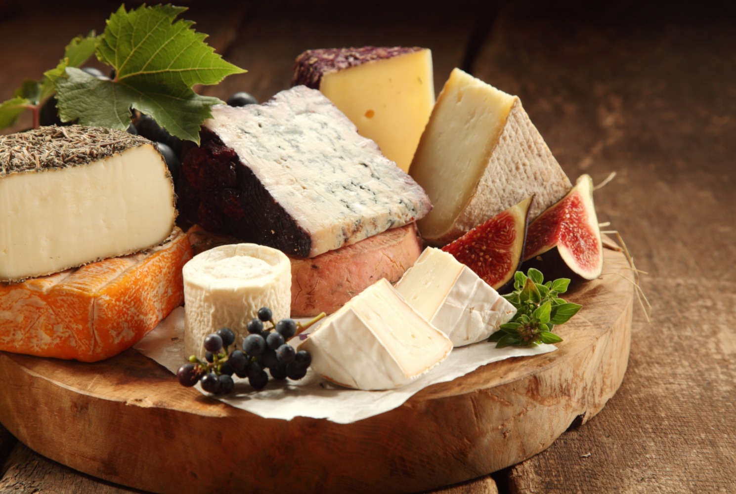 Delicious gourmet cheese platter with a wide assortment of soft and semi-hard cheeses served with sliced sweet fresh figs and grapes on a rustic wooden table with background shadow